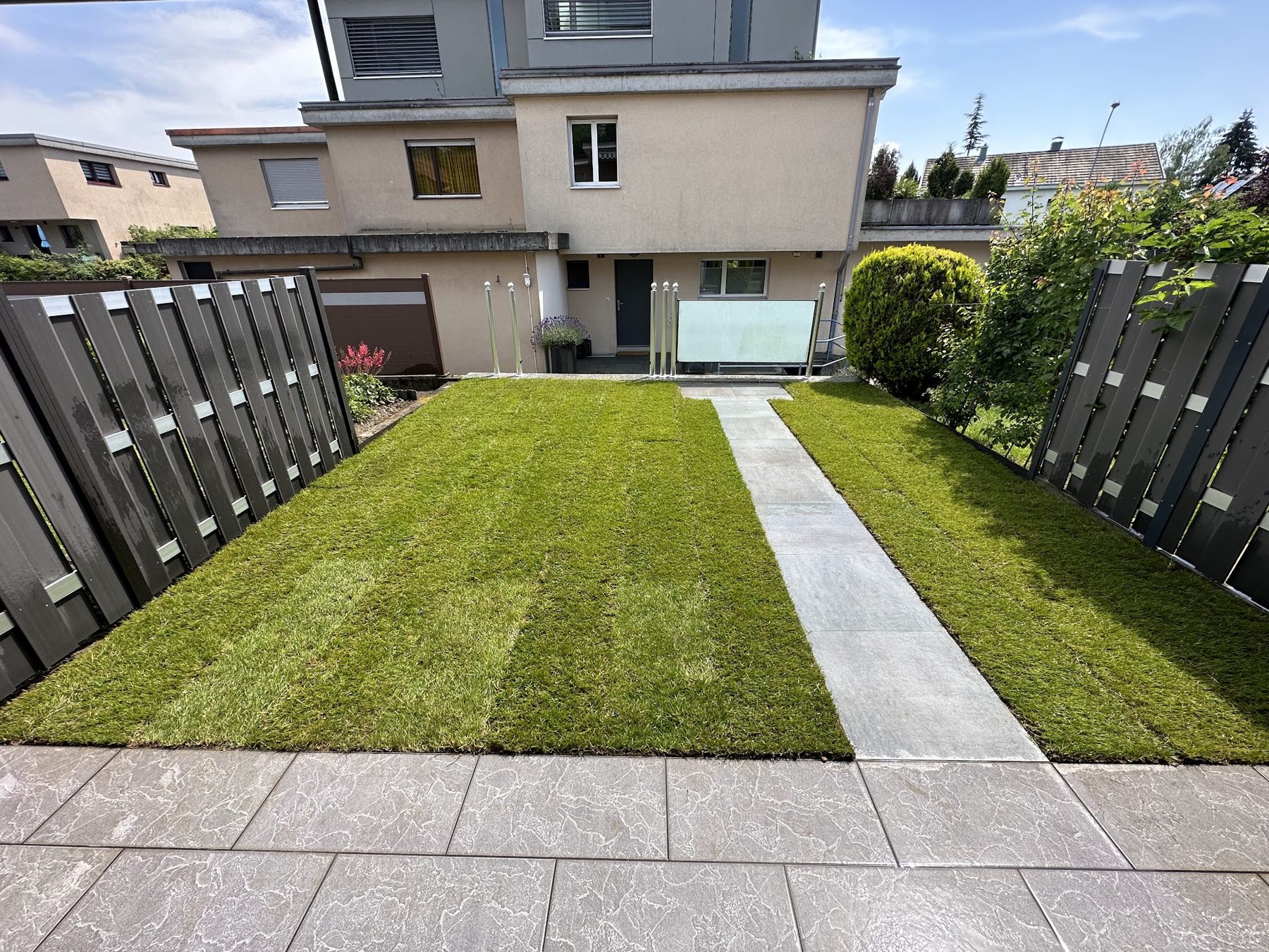 Neuer Rasen mit Plattenweg zum Haus und dunklen Zaunelementen