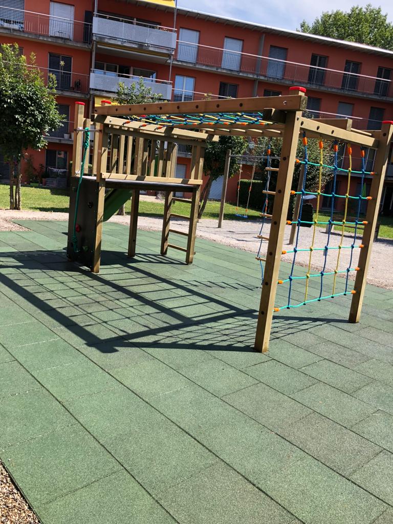 Spielplatz mit Klettergerüst aus Holz auf Fallschutzbelag bei einer Wohnüberbauung