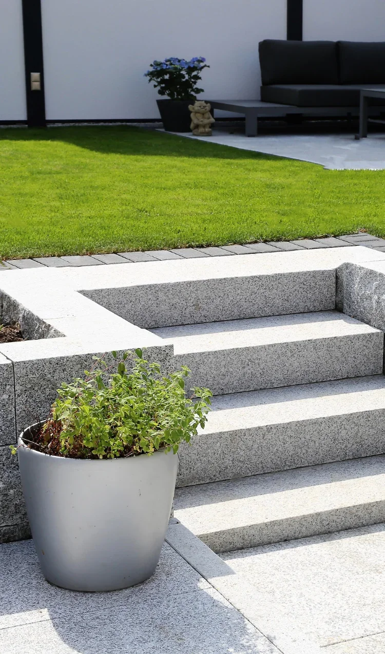 Rasen mit Granittreppe und bepflanztem Topf
