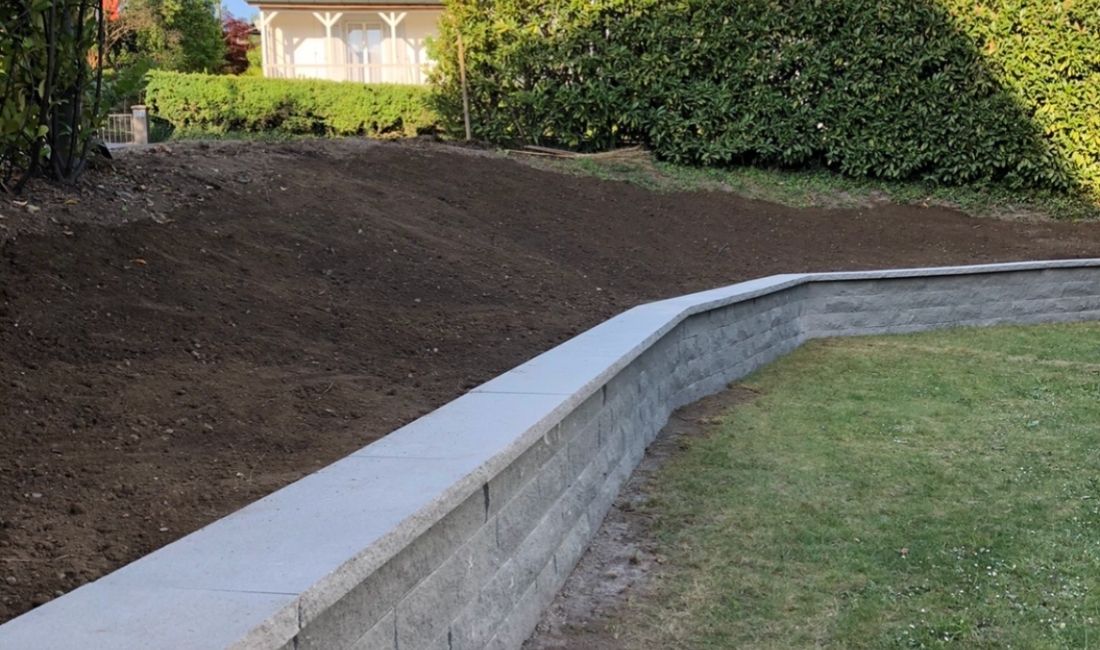 Neue Stützmauer aus Blocksteinen mit frisch planierter Erde