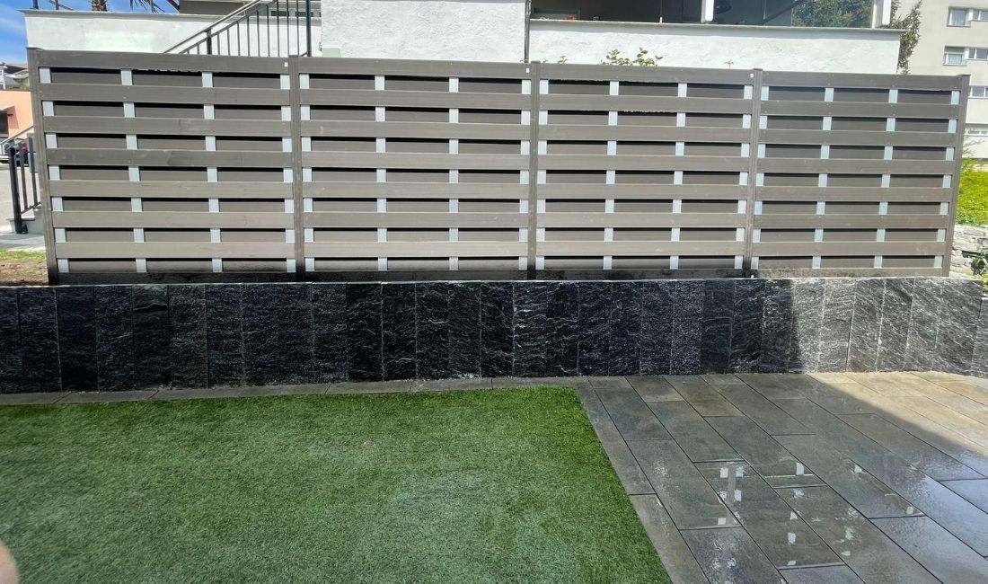 Sichtschutzzaun über Schiefermauer mit Rasen und Plattenbelag